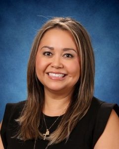 Smiling woman in black top with a cross necklace against a blue studio backdrop