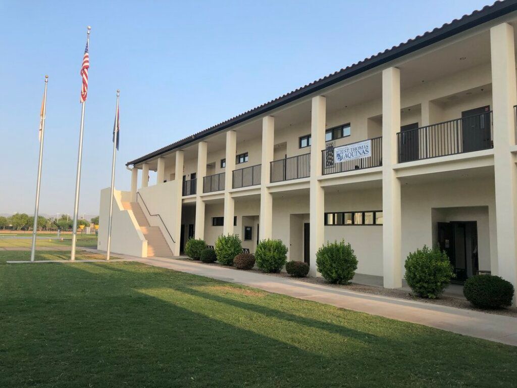 Two-story motel building with white columns, balconies, flags, and a grassy lawn at sunset