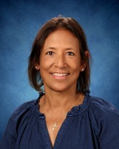 Head-and-shoulders portrait of a smiling person in a navy blouse on a blue studio background