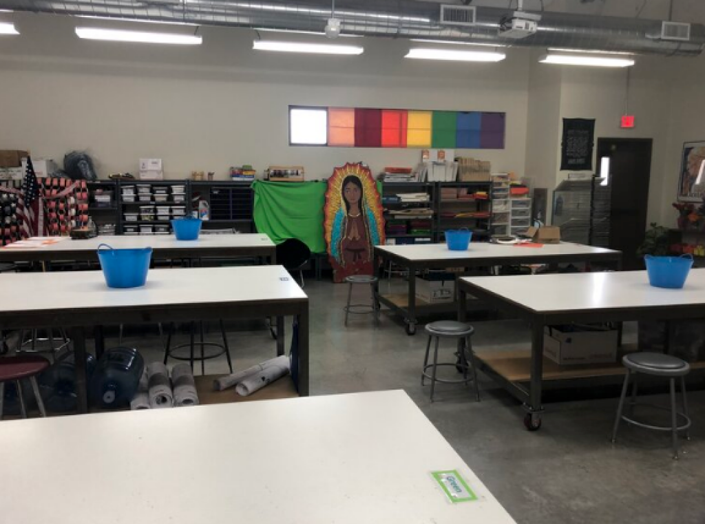 Classroom with tables, blue bins, shelves, and colorful wall panels at the back.