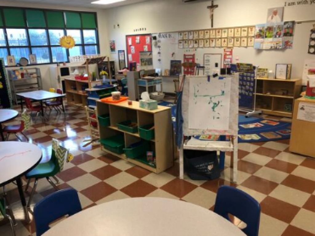 Classroom with tables, chairs, cubbies, and colorful learning materials on a checkered floor.