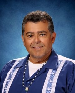 Portrait of a smiling person in a blue robe against a blue studio backdrop