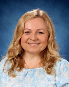 Smiling blonde woman in a light blue floral top against a blue studio backdrop