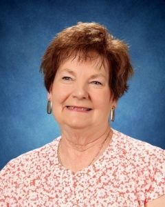 Smiling woman in a pink floral blouse against a blue studio backdrop