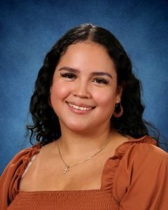 Smiling person in an orange blouse against a blue studio backdrop