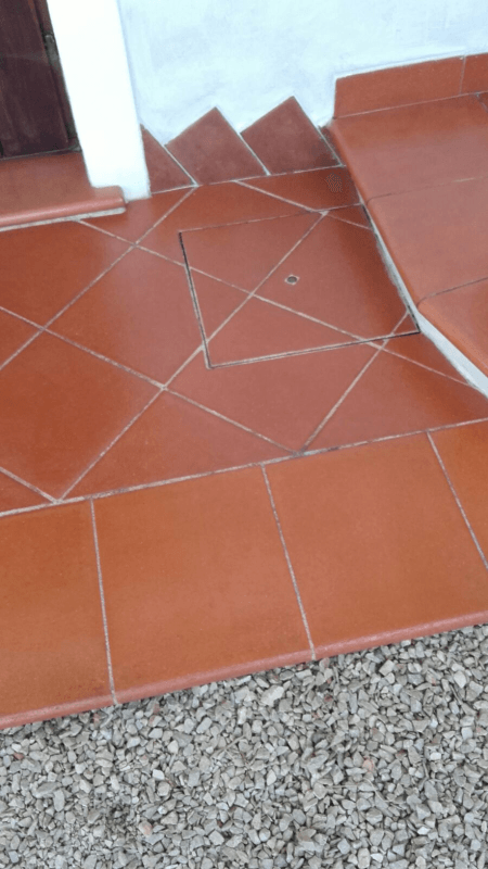 Gradini rivestiti di piastrelle rosse che conducono a una porta, con un motivo di linee collegate e una piccola area di ghiaia sottostante.