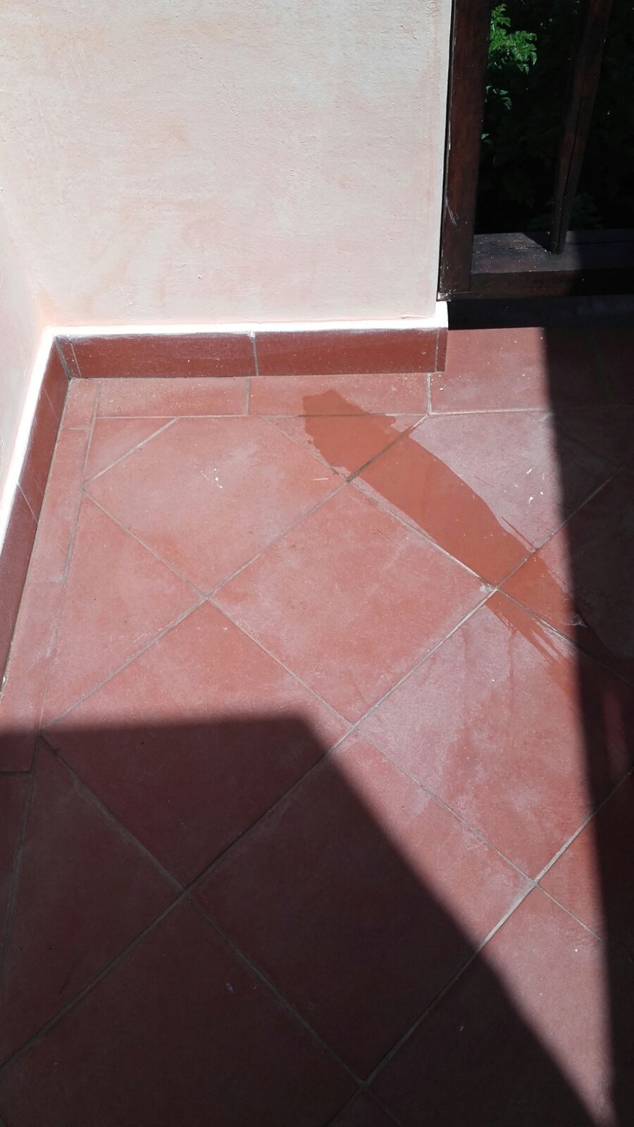 Patio piastrellato di rosso con ombra proiettata da un balcone. Muro rosa sulla sinistra.