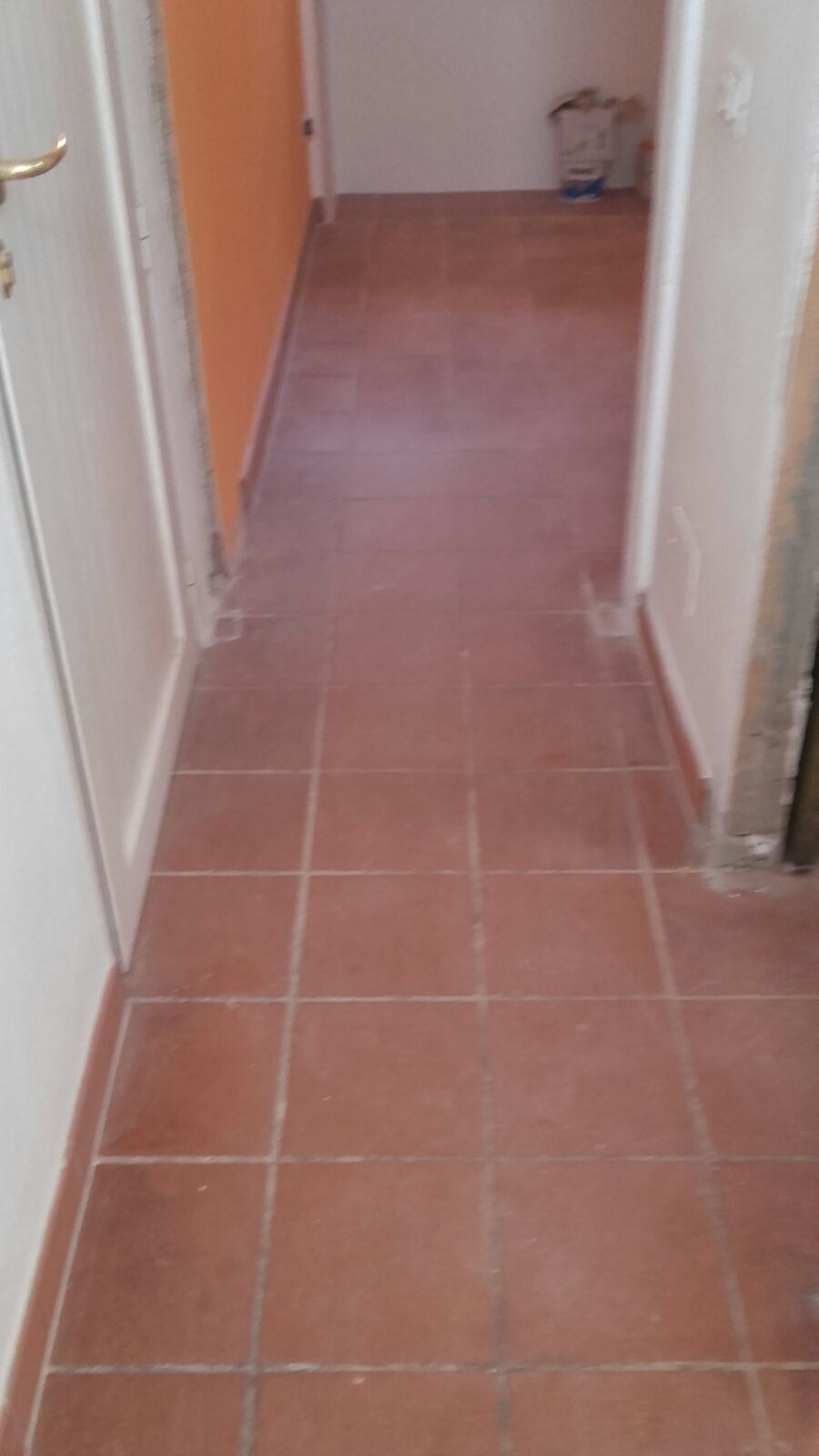 Corridoio piastrellato marrone con stipiti delle porte bianchi e parete arancione, che conduce a un'altra porta.