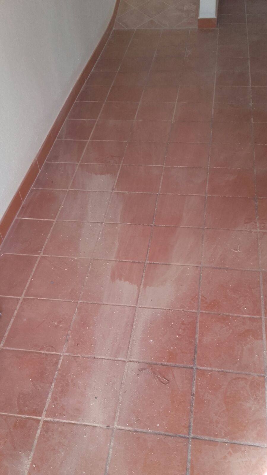 Pavimento piastrellato rosso in una stanza, con pareti bianche e battiscopa rossastro.