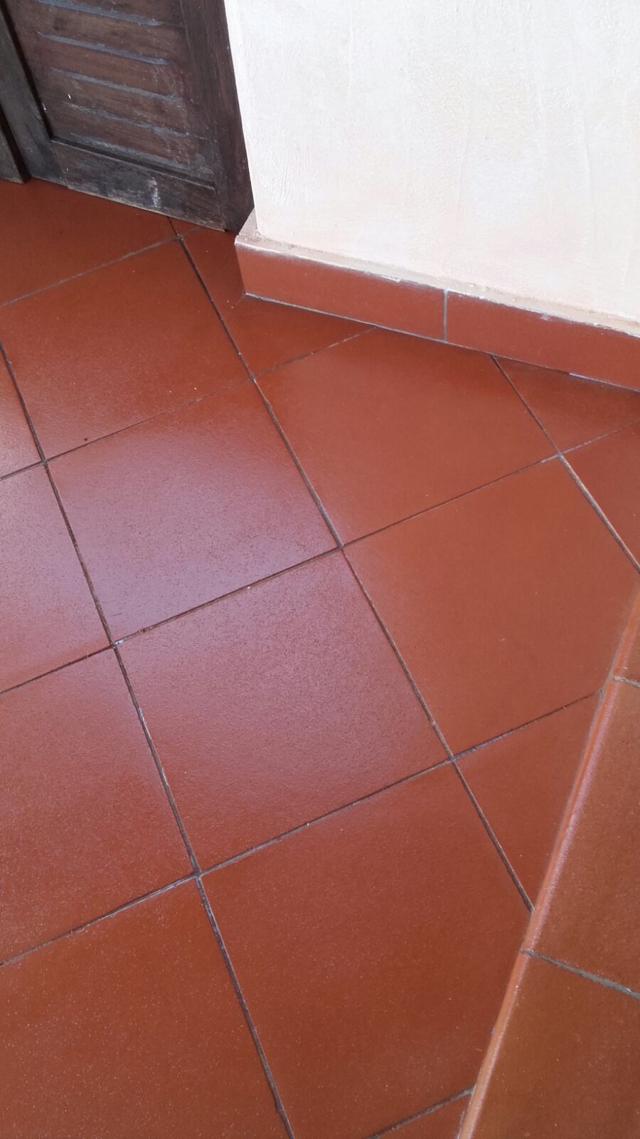 Pavimento piastrellato rosso-marrone accanto a una parete bianca con battiscopa marrone.