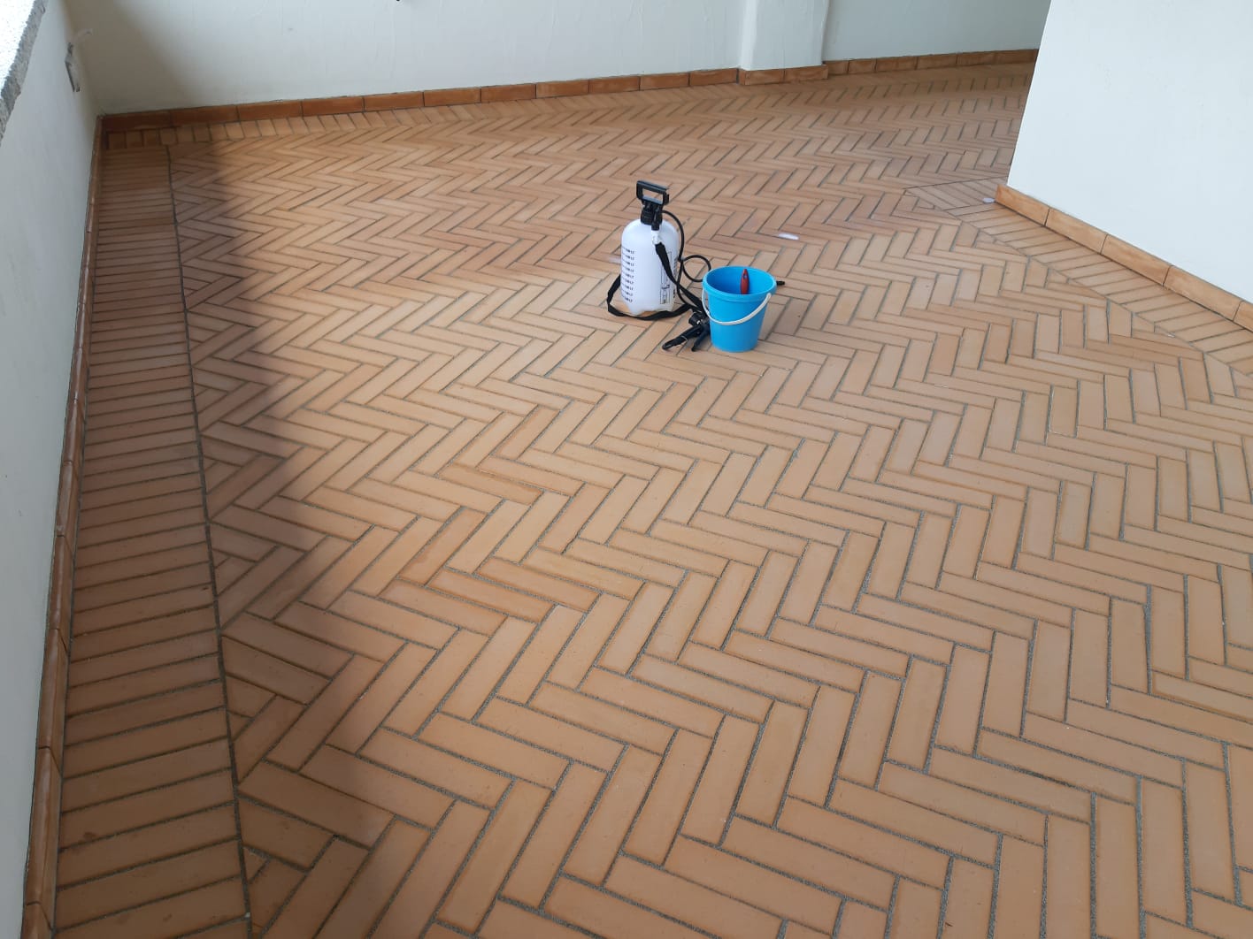 Pavimento in mattoni con motivo a spina di pesce; sul pavimento ci sono un flacone spray e un secchio.