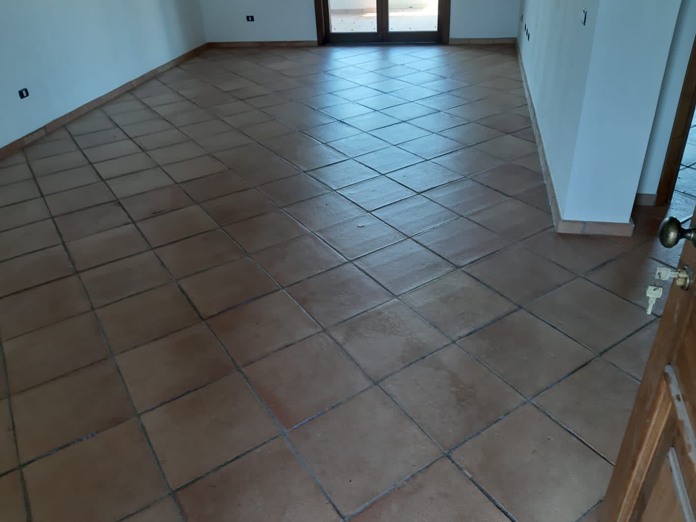 Pavimento in piastrelle marroni in una stanza, con una porta parzialmente visibile sulla destra.