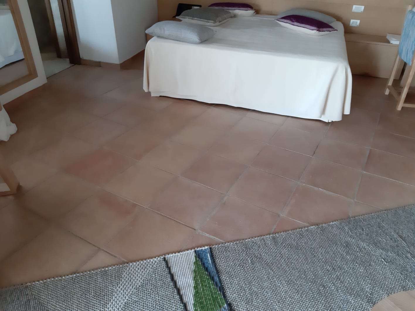 Camera da letto con letto, pavimento in cotto e tappeto con dettagli verdi.