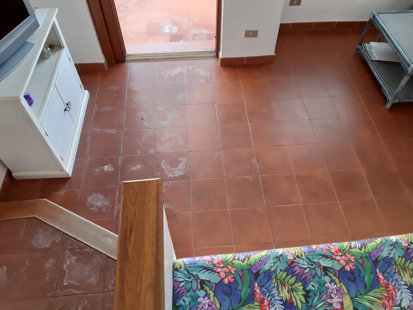 Pavimento in piastrelle di terracotta in una stanza, con un mobile bianco, una porta aperta e un divano decorato.
