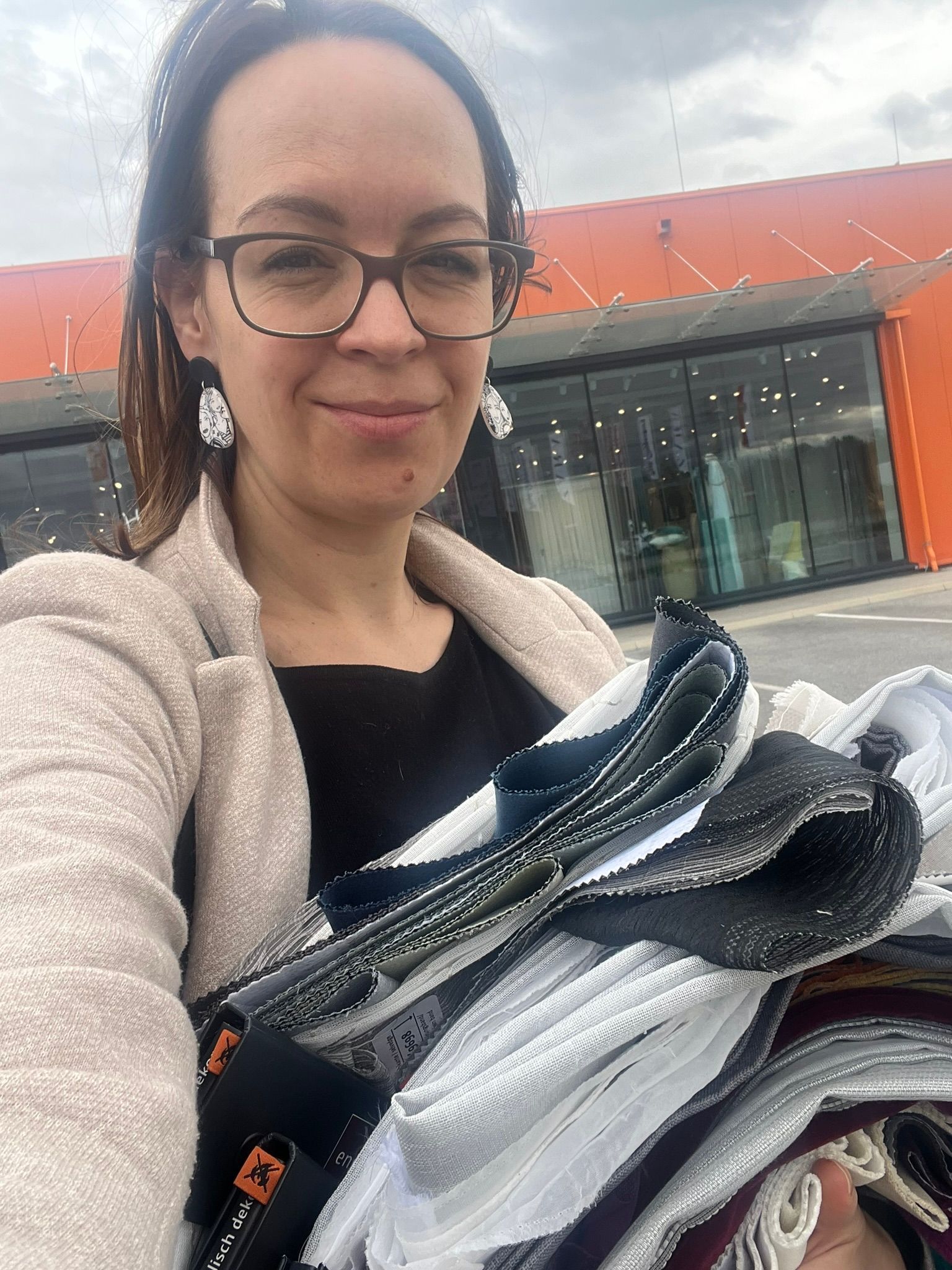 Frau hält Stoffe in der Hand und lächelt vor einem Gebäude.