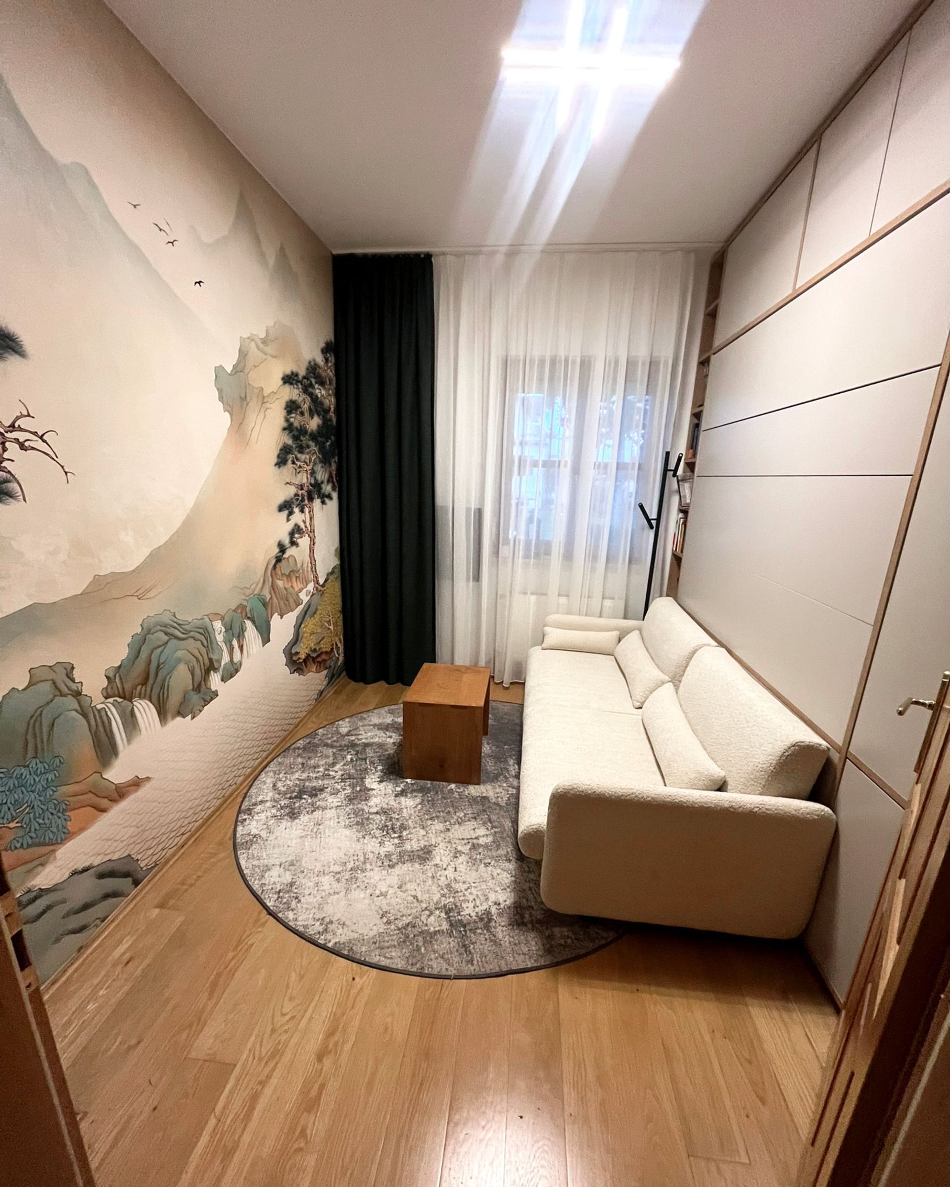 Beiges Sofa in einem Zimmer mit hellem Holzboden, einem gemusterten Teppich und einer hellen Akzentwand.