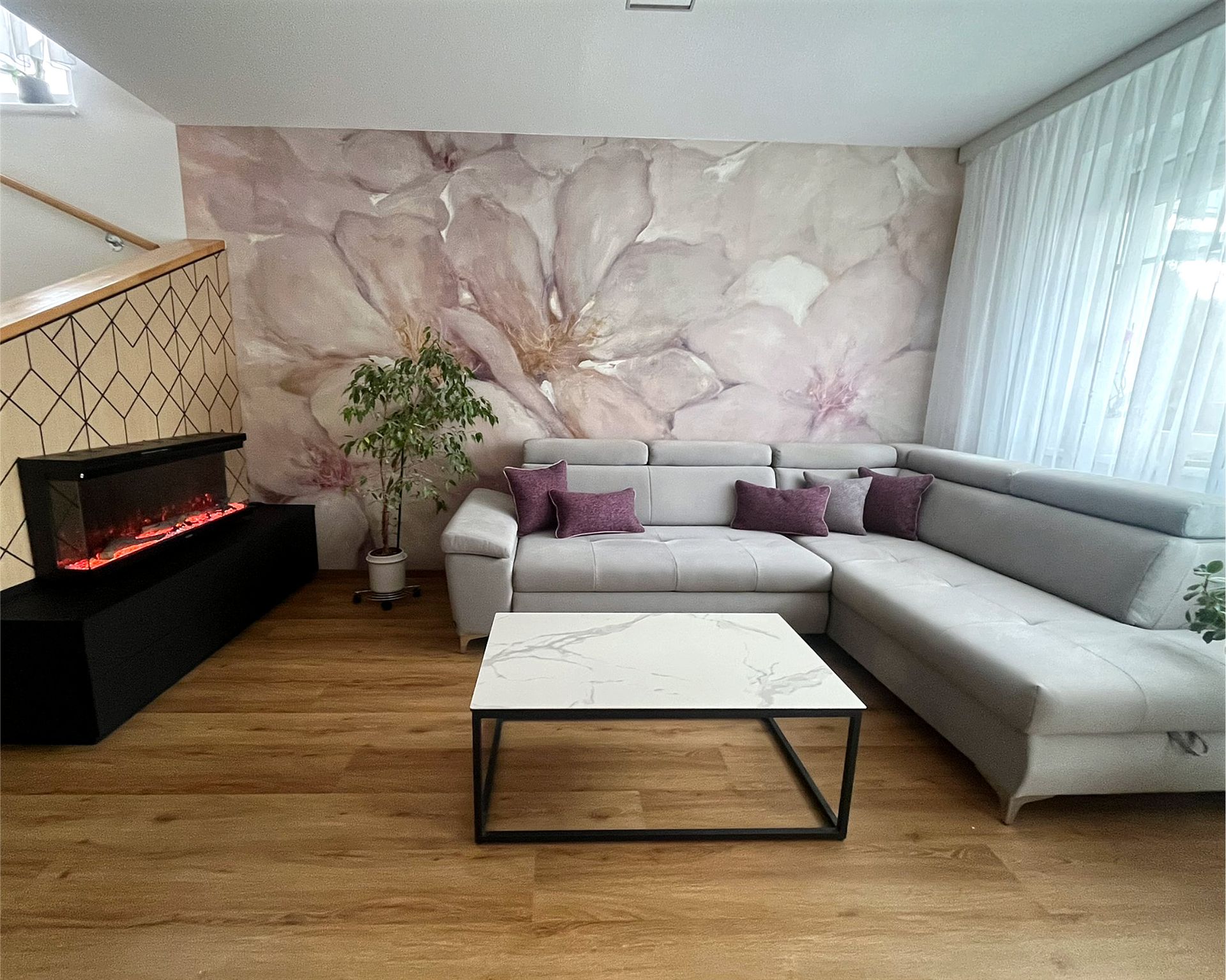 Wohnzimmer nach der Neugestaltung mit floraler Designtapete, Ecksofa und Design-Heizkamin