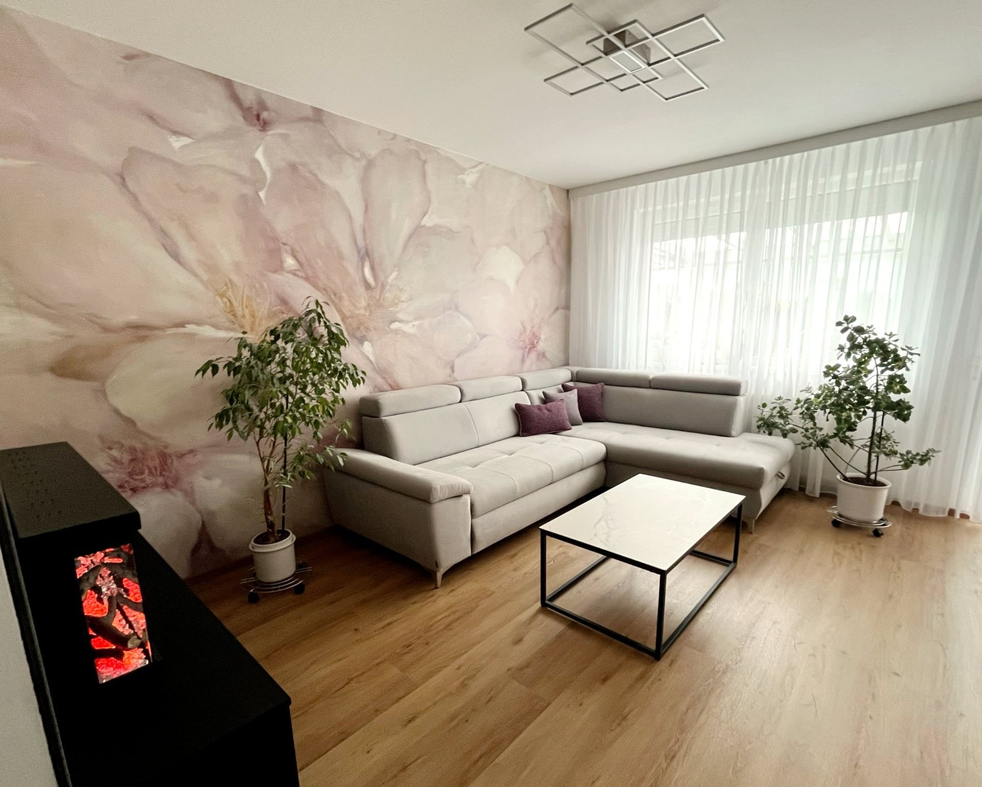 Wohnzimmer nach dem Umbau mit floraler Wandgestaltung, Design-Heizkamin und gemütlicher Wohnatmosphäre