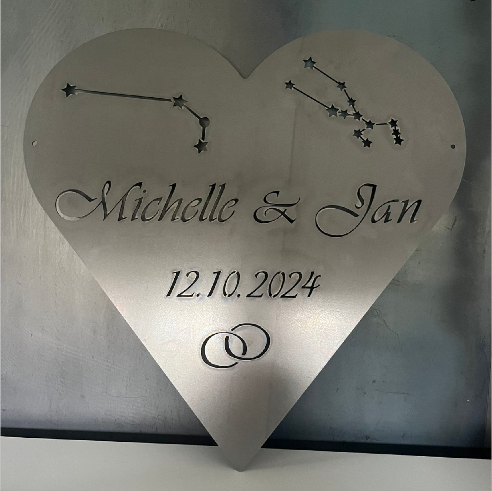 Silbernes herzförmiges Hochzeitsschild mit eingravierten Namen „Michelle & Jan“, Datum „12.10.2024“,