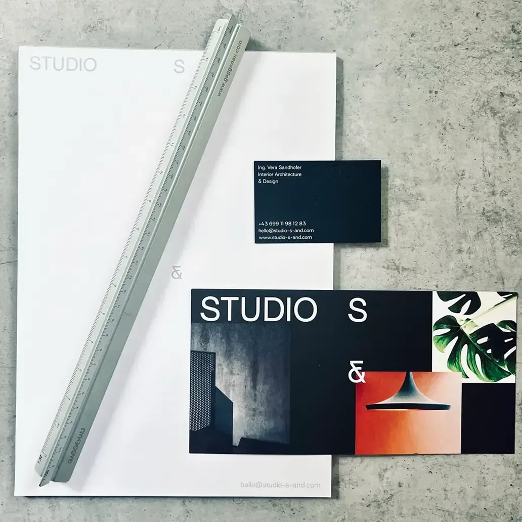Studio S& Branding: Briefpapier mit Logo auf weißem Grund, schwarze Visitenkarten, Lineal auf Beton.