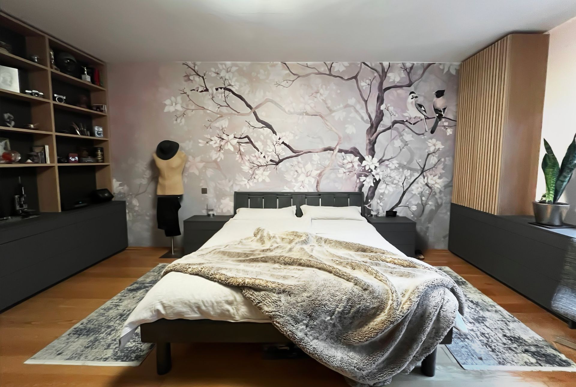 Modernes Schlafzimmerdesign mit großformatiger Blütentapete, anthrazitfarbenem Bett und maßgefertigten Lamellenfronten in Eiche