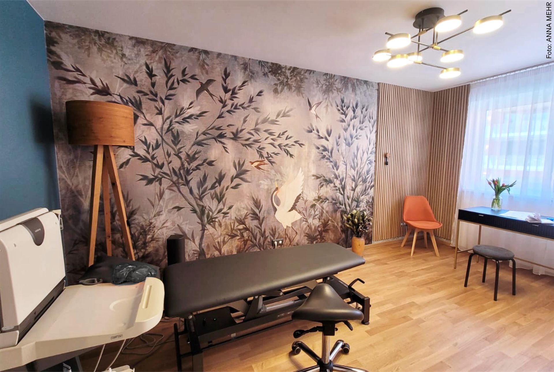 Moderne Physiotherapie-Praxis mit großformatiger Naturtapete, schwarzer Behandlungsliege, Eichenboden und wohnlicher Beleuchtung