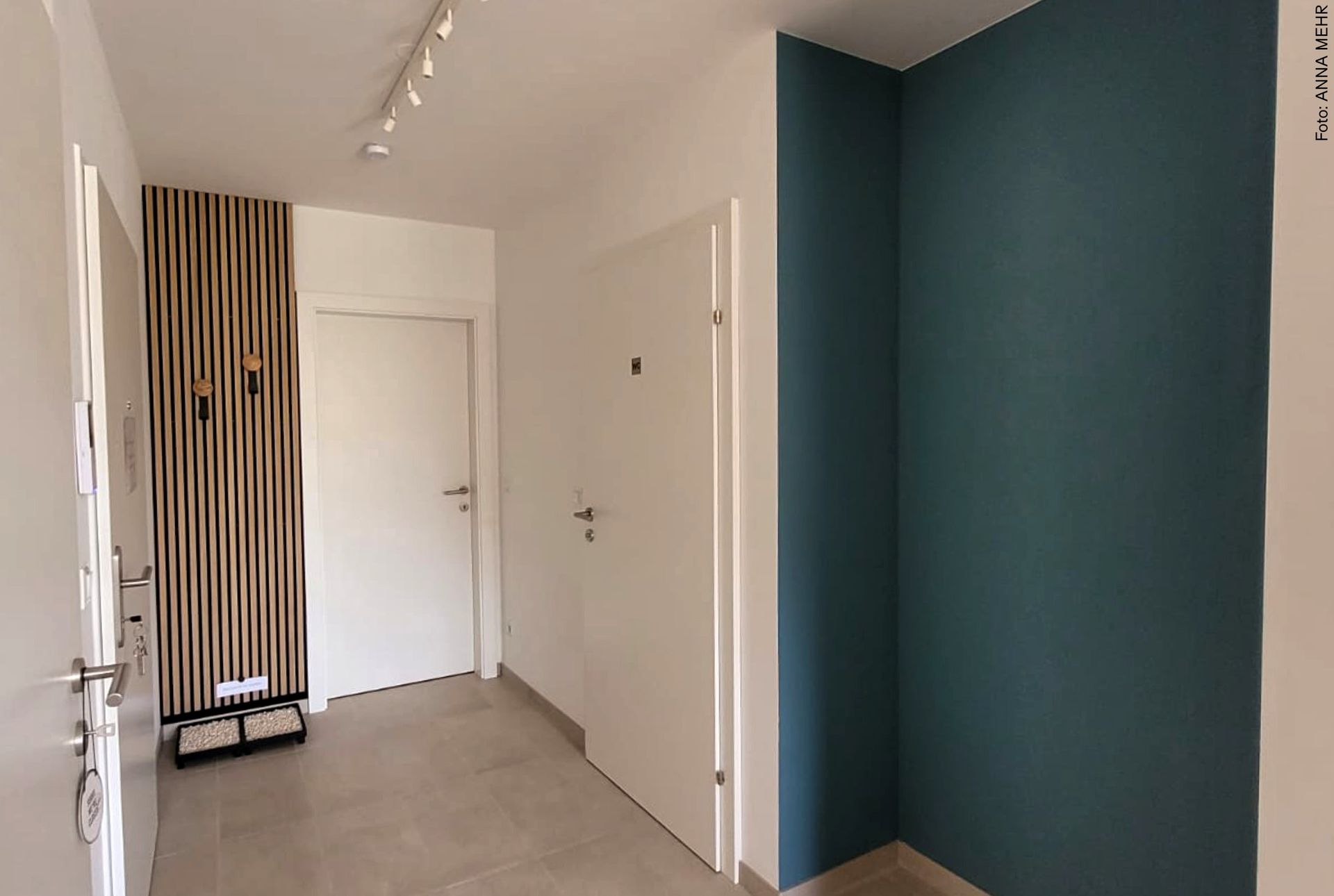 Eingangs- und Wartebereich der Praxis mit petrolblauer Wand, heller Garderobe, Akupaneelen aus Holz und minimalistischer Gestaltung