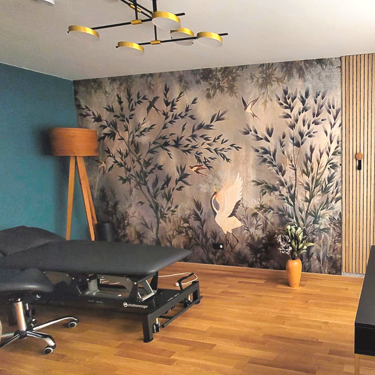 Behandlungsraum: Massageliege, Blumenwandbild, Holzboden, türkisfarbene Wand und Holzlattenwand.
