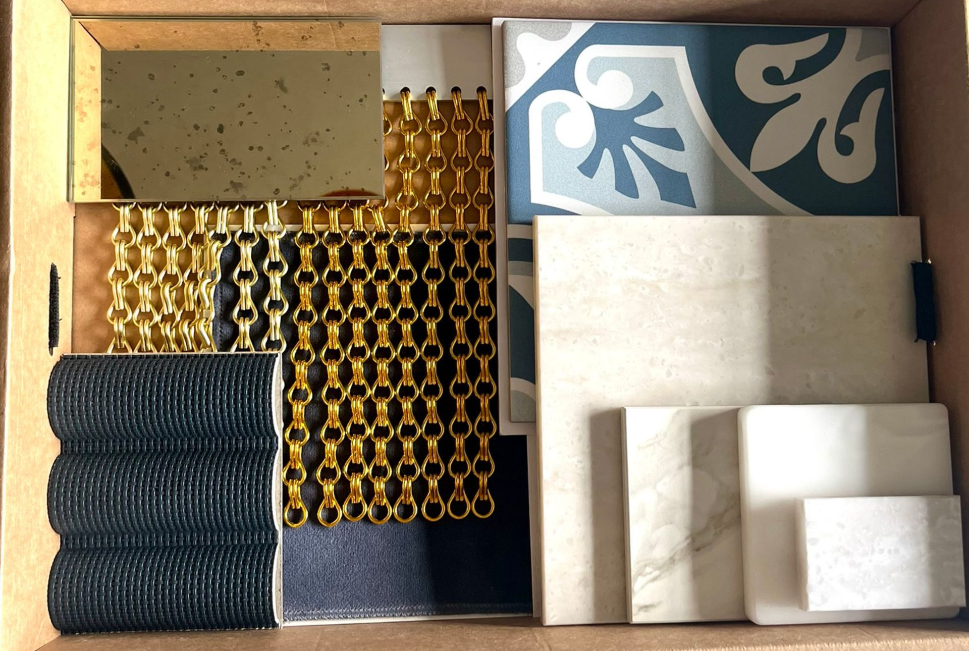Materialcollage für exklusives Shopdesign mit Messingkettenvorhang, Naturstein, dunklen Stoffen und hochwertigen Oberflächen