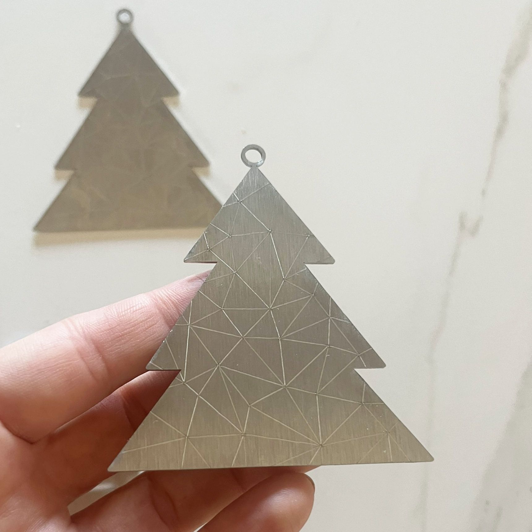 Eine Hand hält einen metallenen Weihnachtsbaumschmuck mit geometrischem Muster;