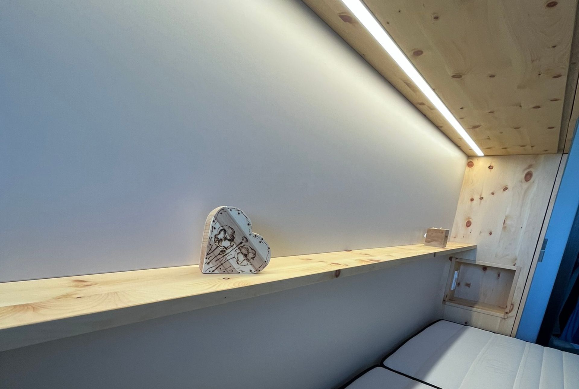 Integrierte Nachttisch-Nische aus Zirbenholz mit indirekter Beleuchtung und warmem sandbeigen Wandpaneel im Schlafzimmerdesign