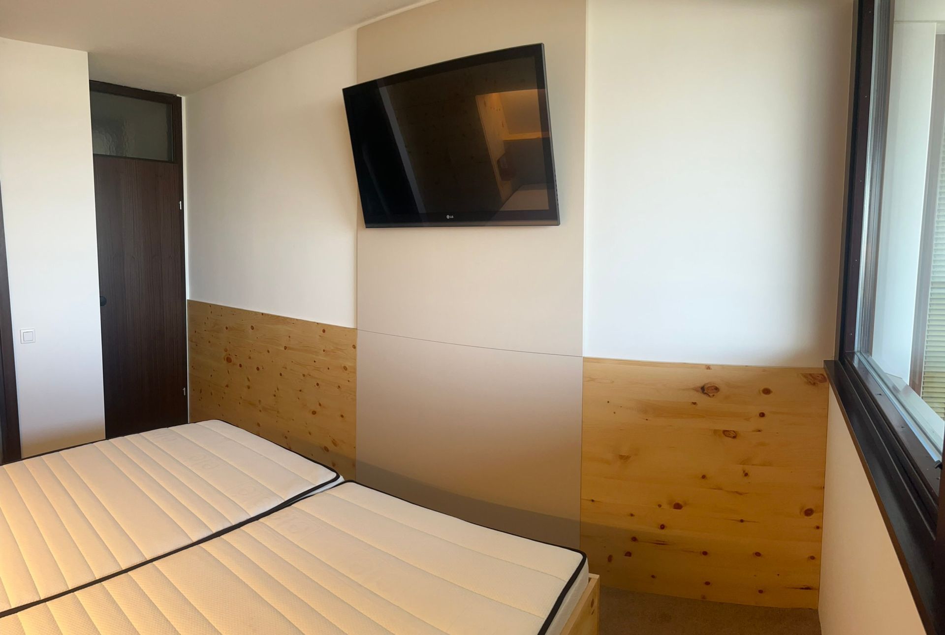 Modernes Schlafzimmer mit TV-Wandpaneel in Sandbeige, Zirbenholz-Verkleidung und reduziertem Hotelzimmer-Charakter