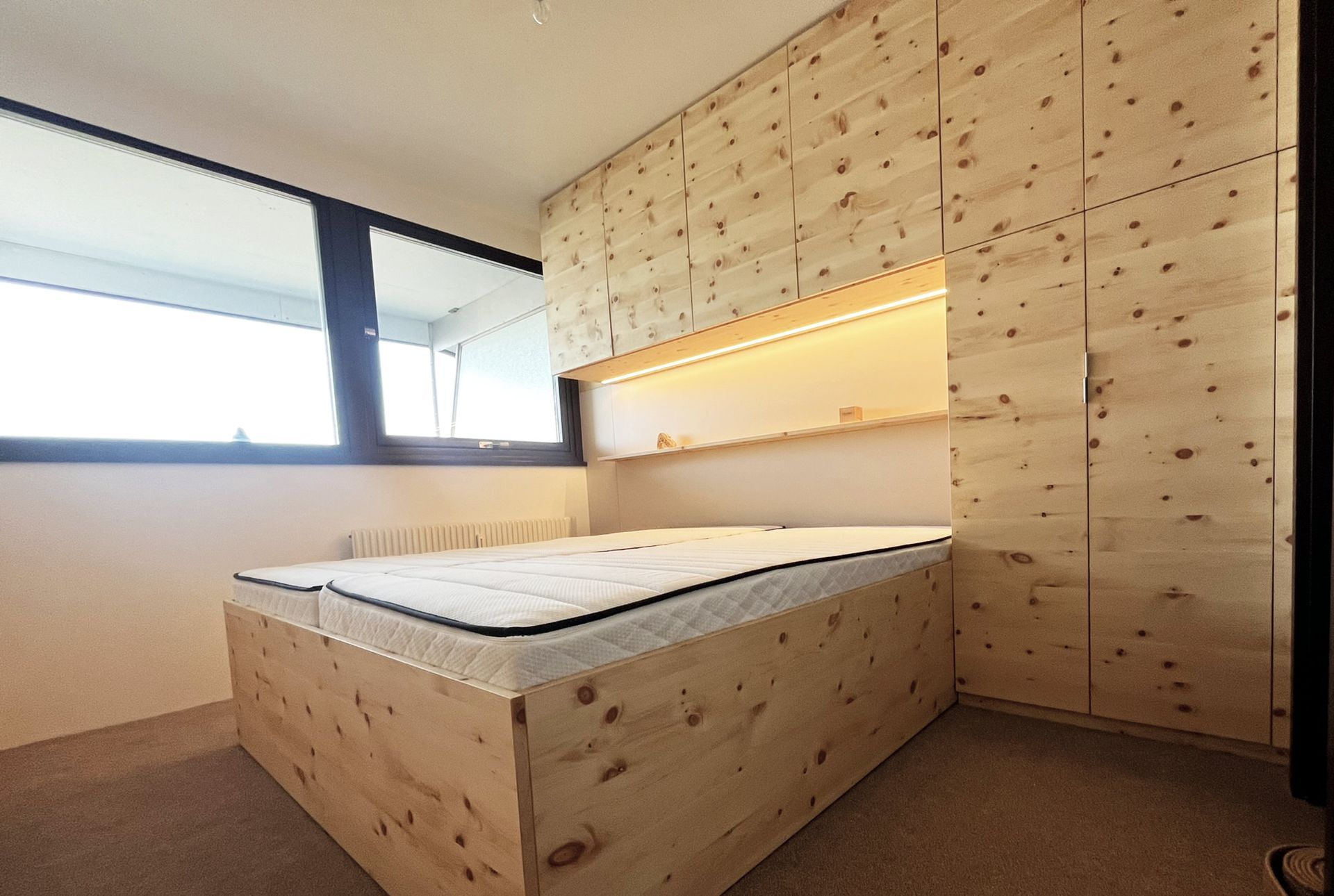 Modernes Zirbenschlafzimmer mit maßgefertigtem Stauraumbett, indirekter Beleuchtung und grifflosen Zirbenfronten in Wien Liesing