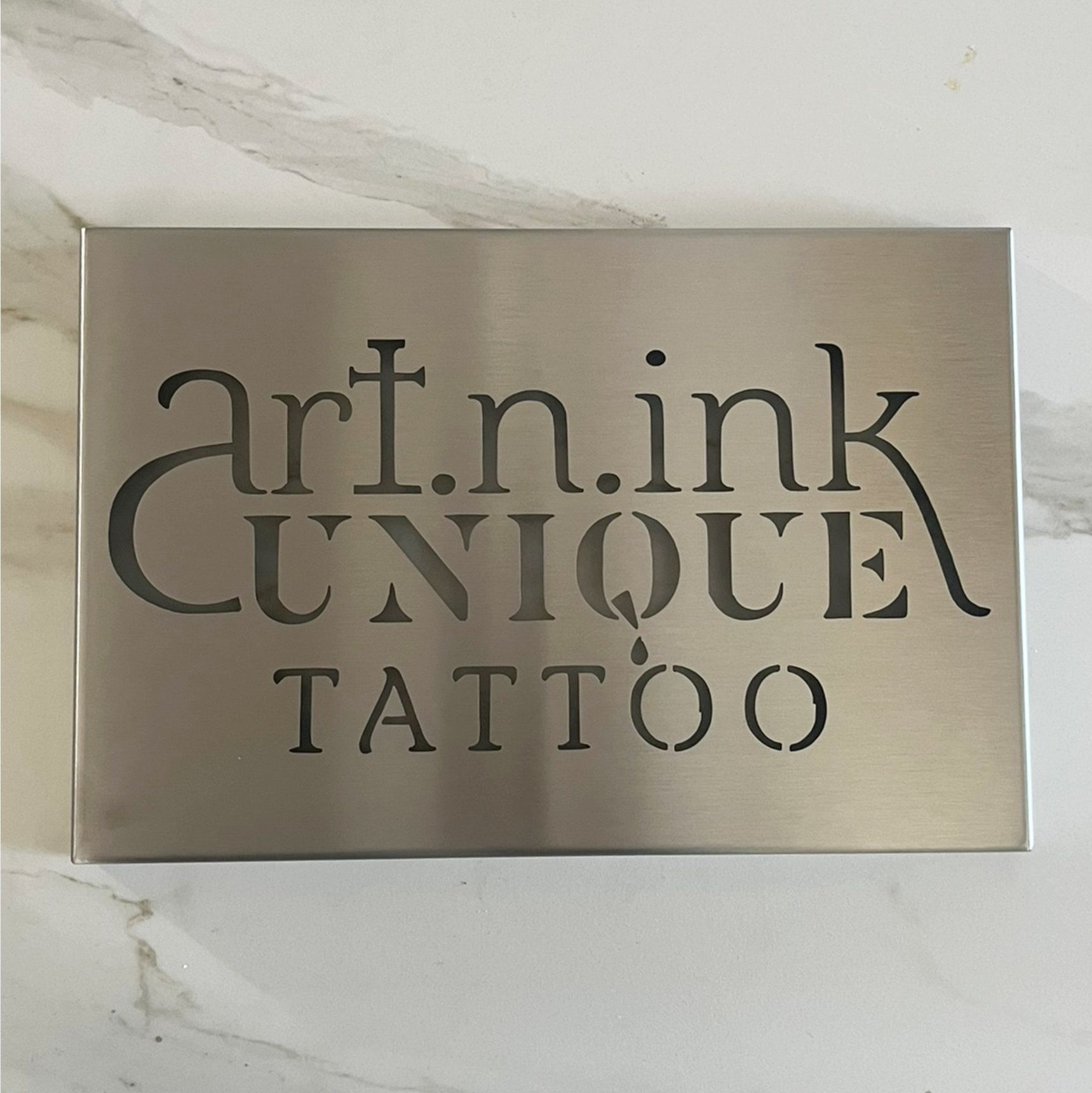 Metallschild mit ausgestanzten Buchstaben für „art.n.ink UNIQUE TATTOO“.