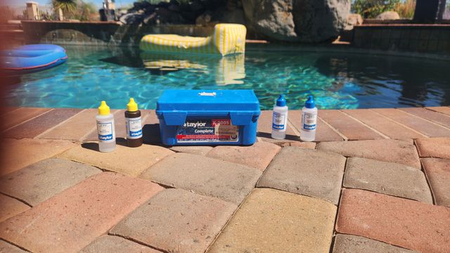Person holding pool water test strips and bottles beside a swimming pool