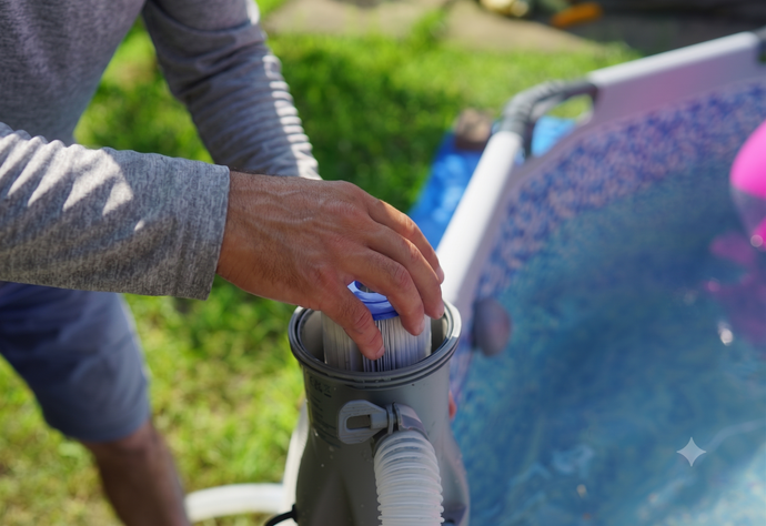 Hand placing a pool vacuum hose into a swimming pool, with blue water and patio stones nearby
