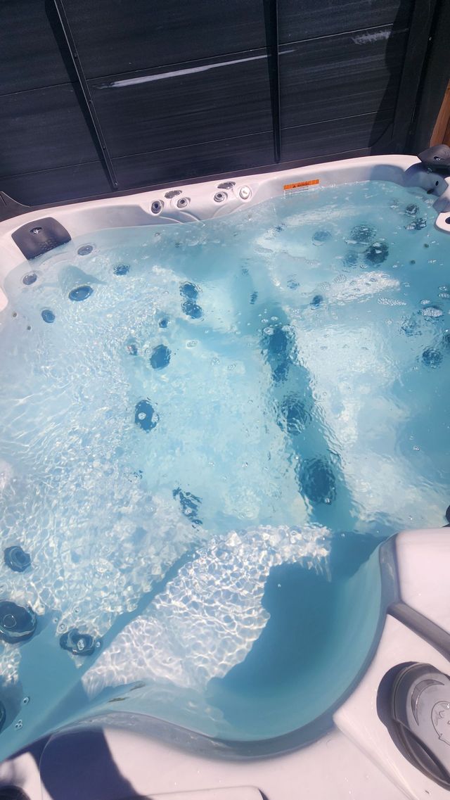 Man cleaning a hot tub, reaching into the water beside a white spa outdoors
