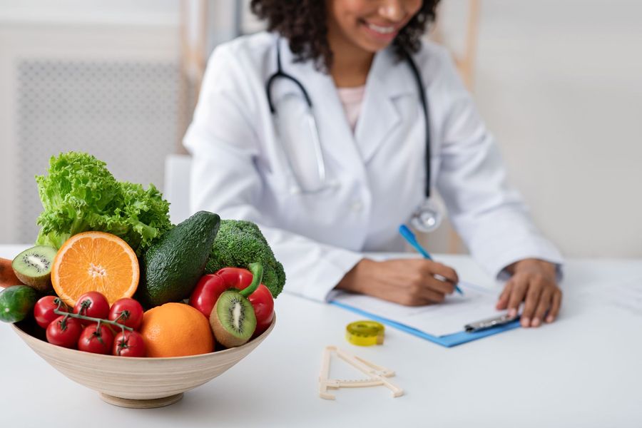 A Doctor in a White Coat Typing at a Desk with a Fruit Bowl