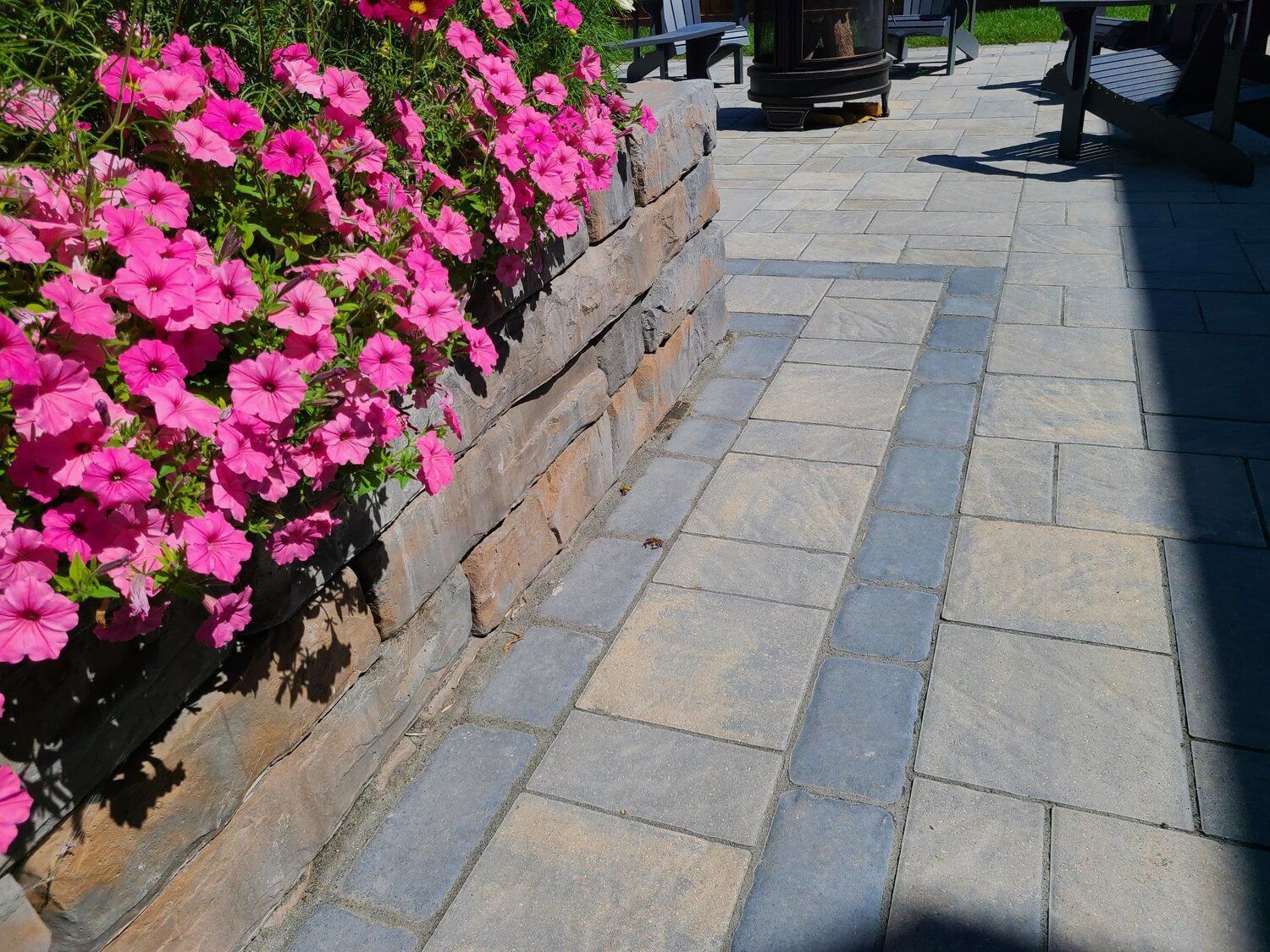 A brick walkway with pink flowers on the side of it
