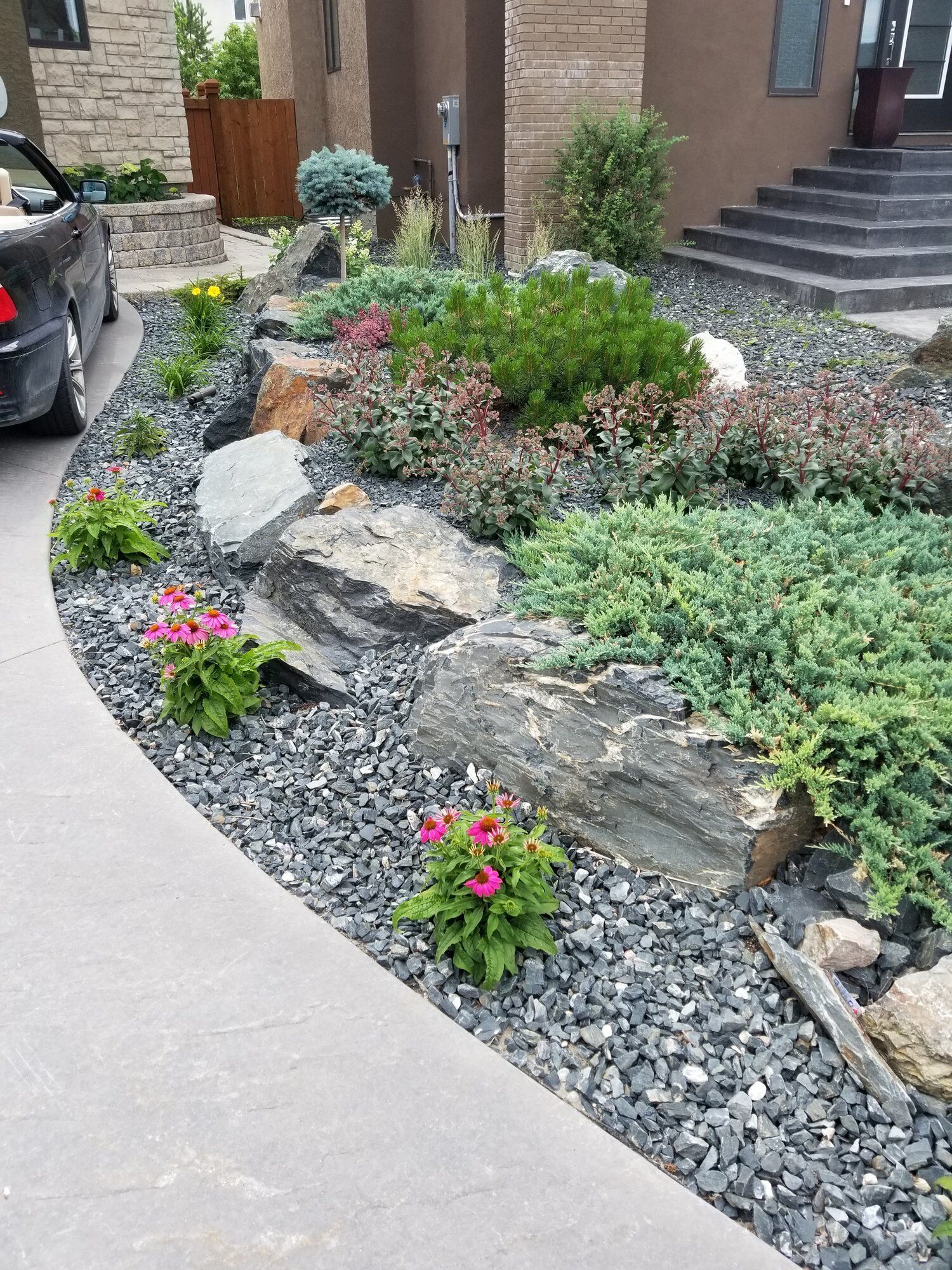 A car is parked in a driveway next to a garden.