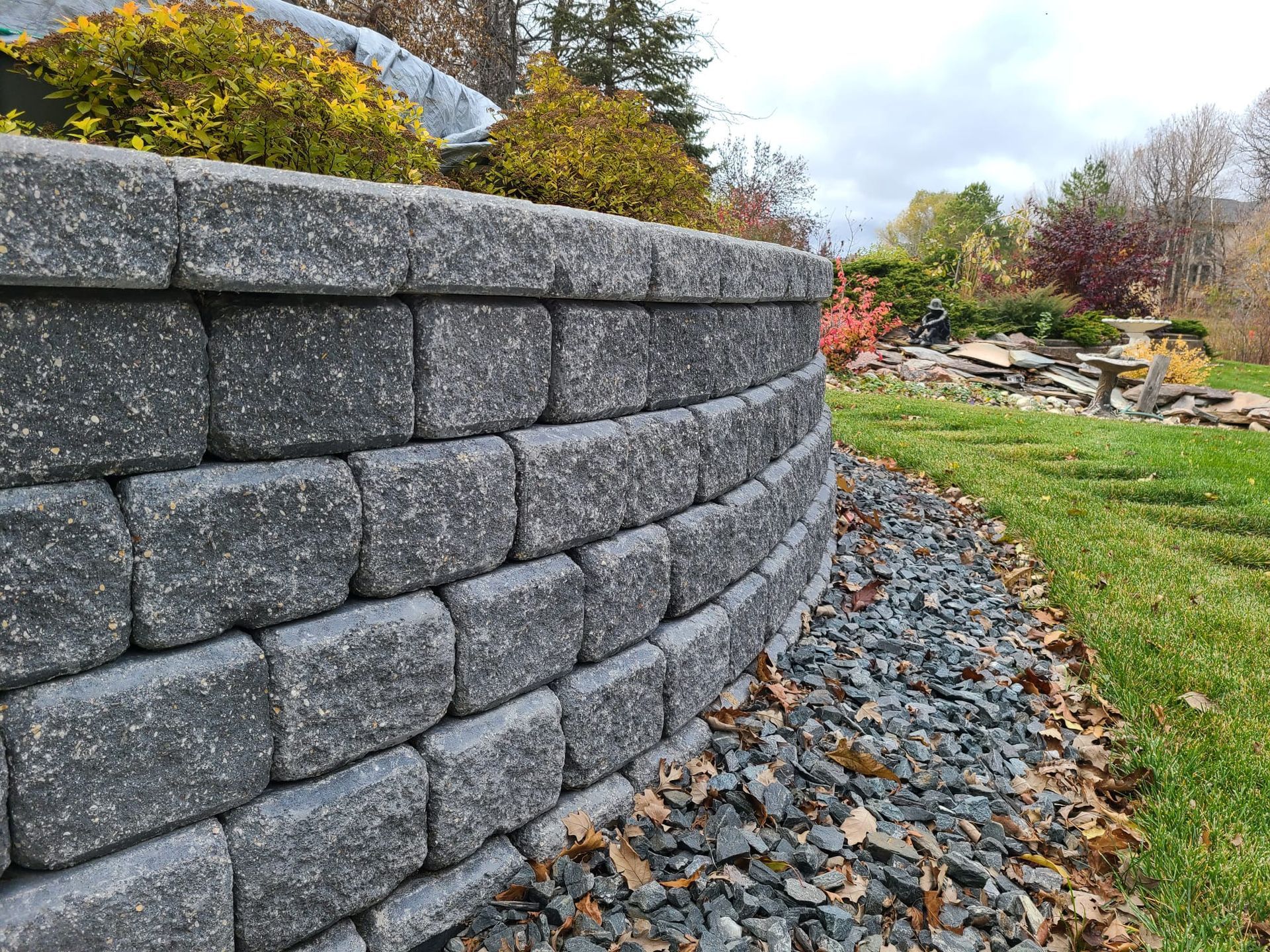 A retaining wall is surrounded by stone and grass in a garden.