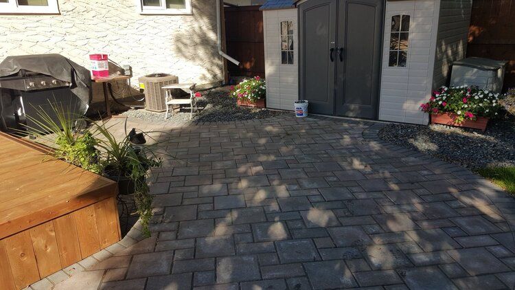 A paver patio with a grill and a shed in the backyard