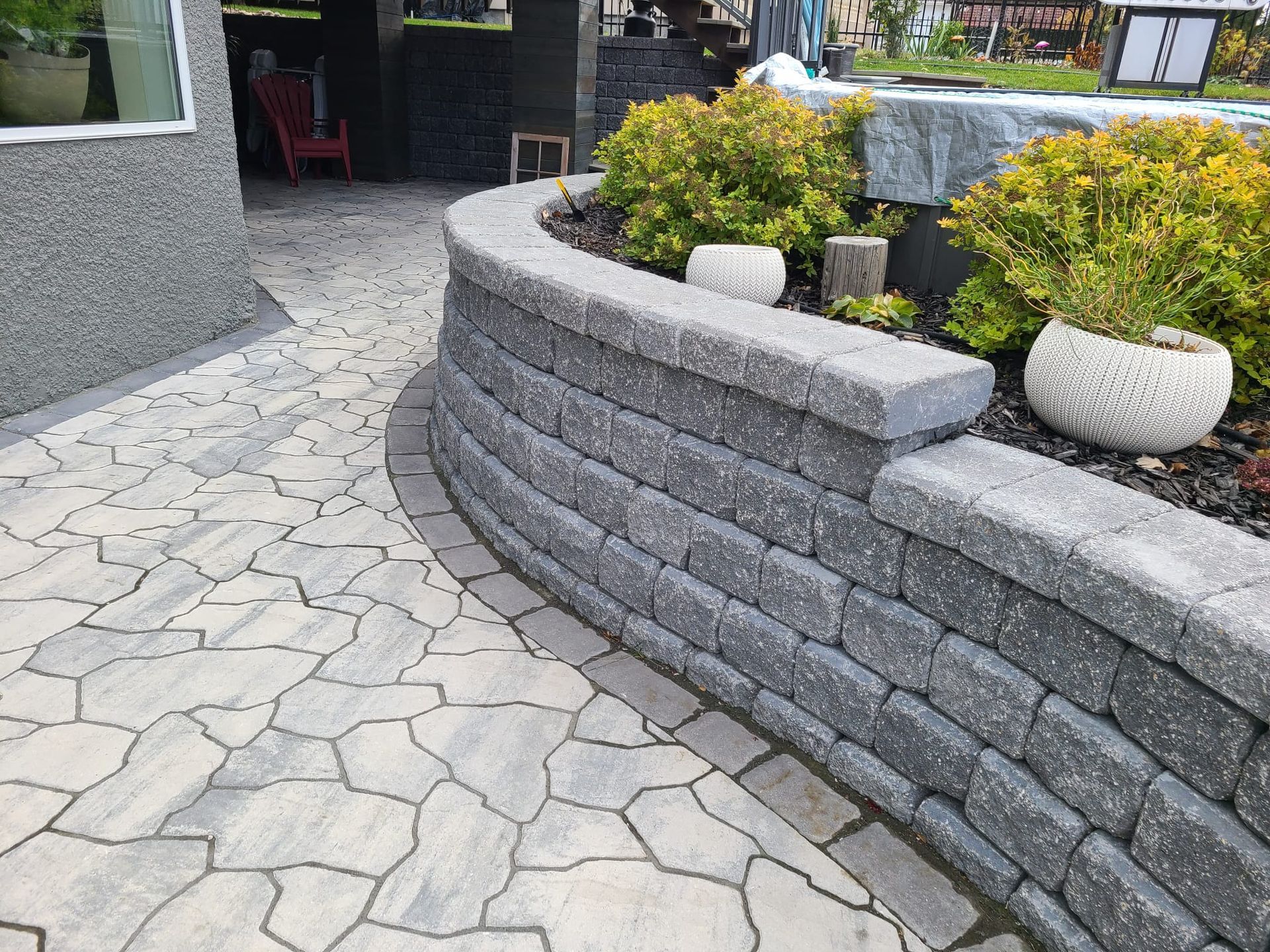 A stone retaining wall surrounds a patio with potted plants.