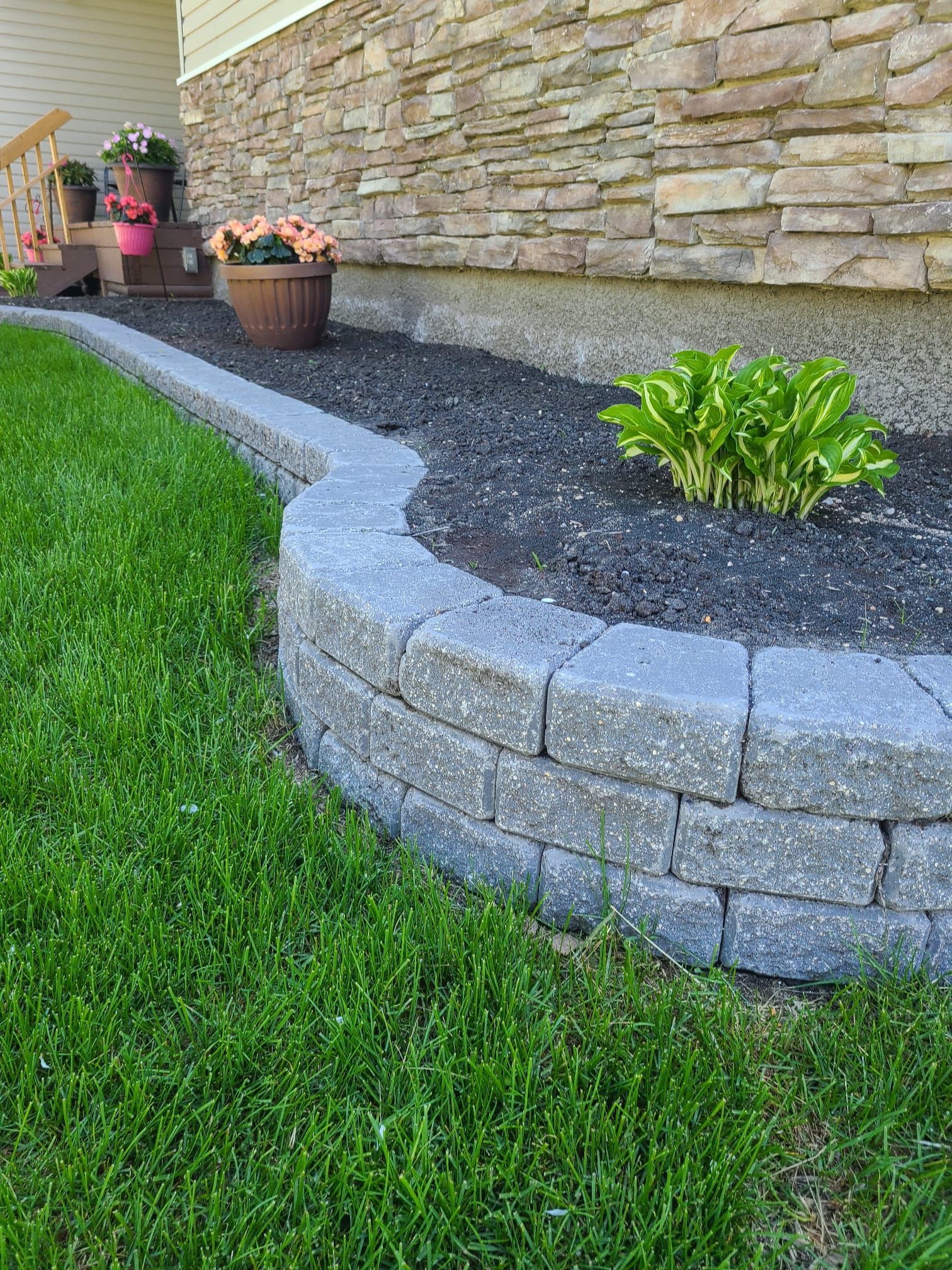 A stone wall surrounds a lush green lawn in front of a house.