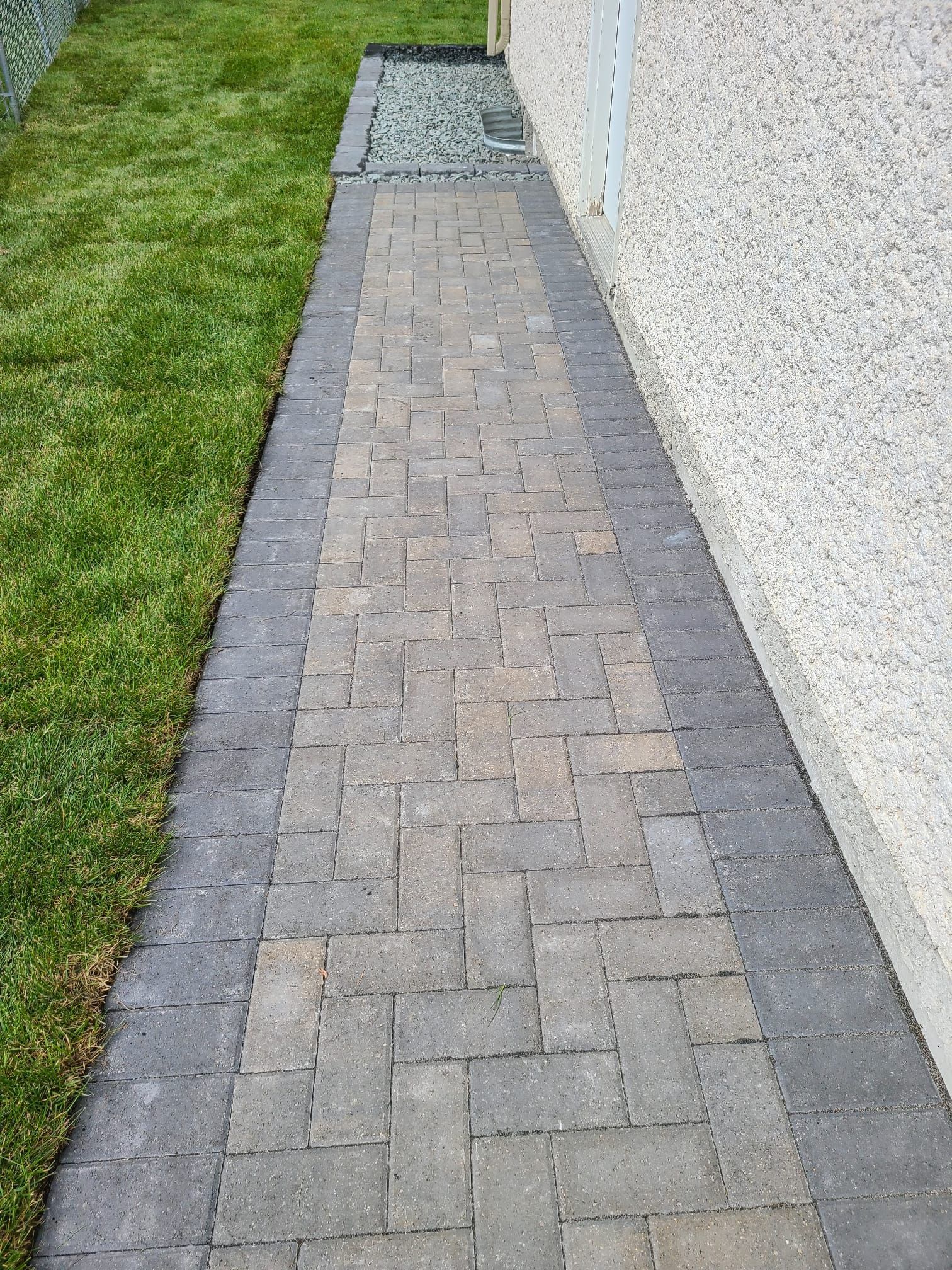A brick walkway leading to a building next to a lush green lawn.