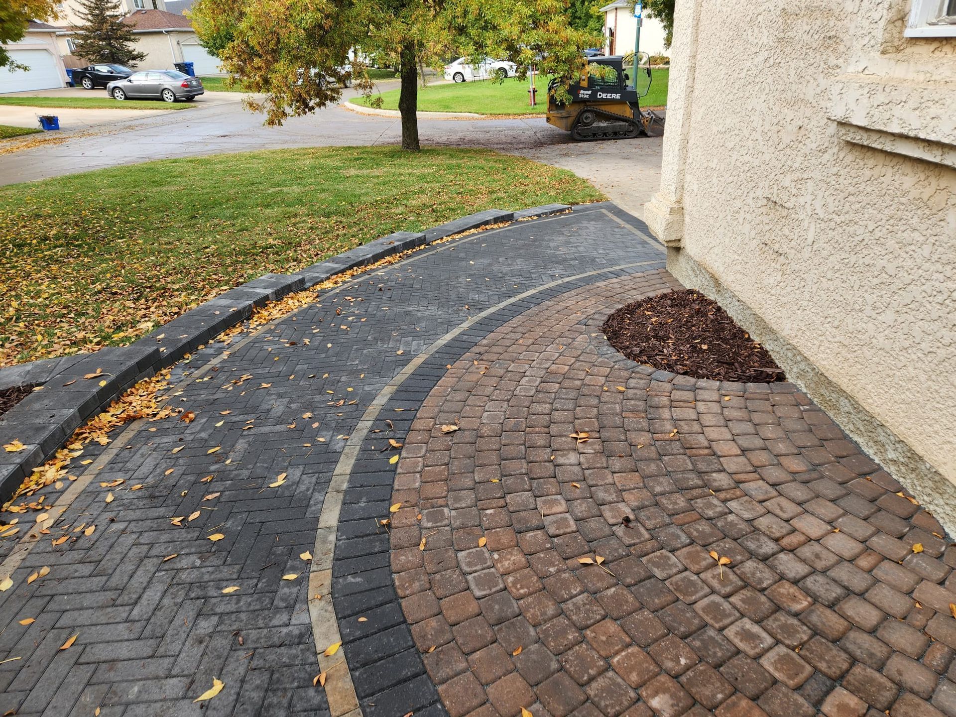 A brick walkway leading to a house with a bulldozer in the background.
