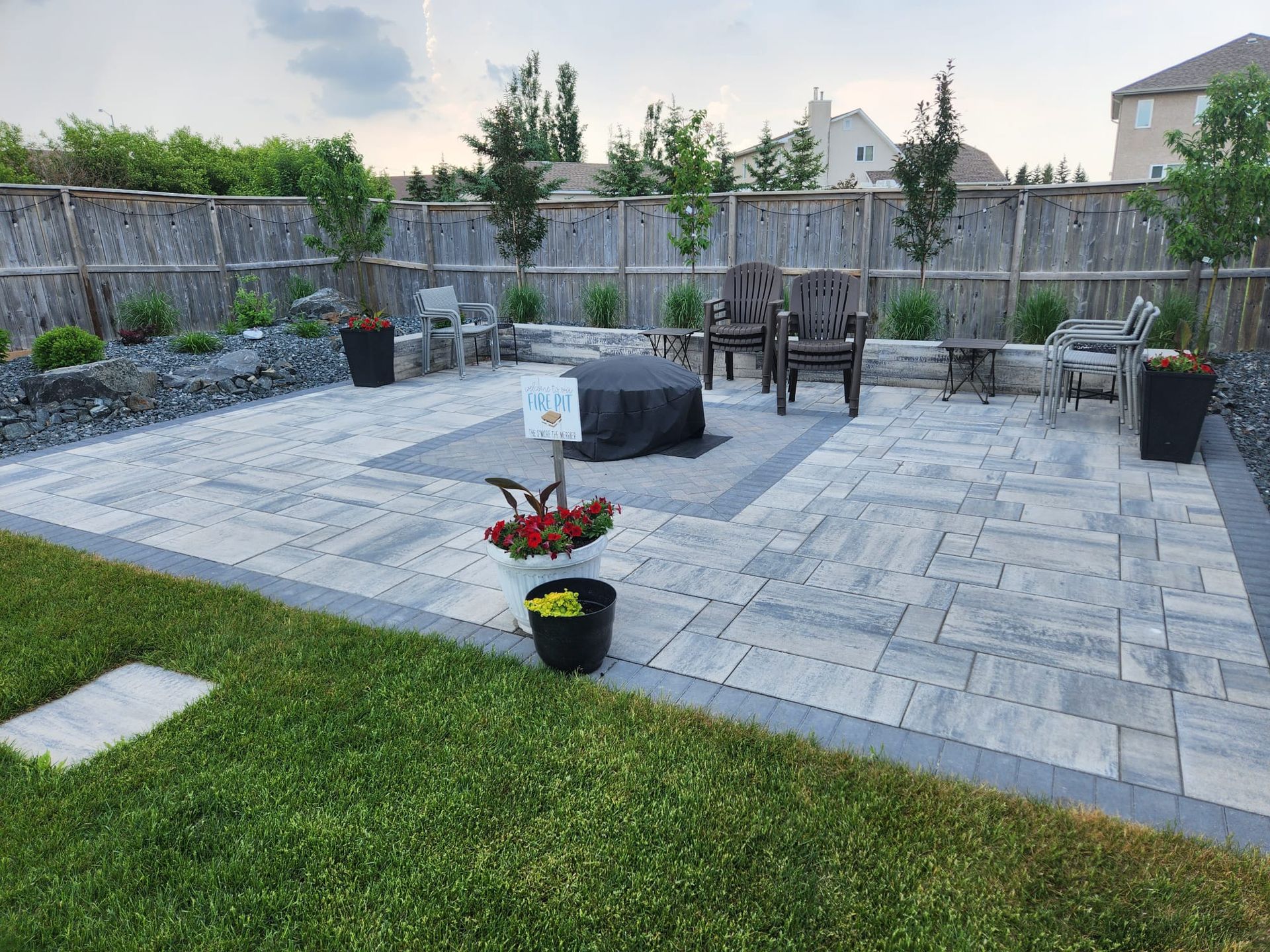 A patio with a fire pit and chairs in a backyard.