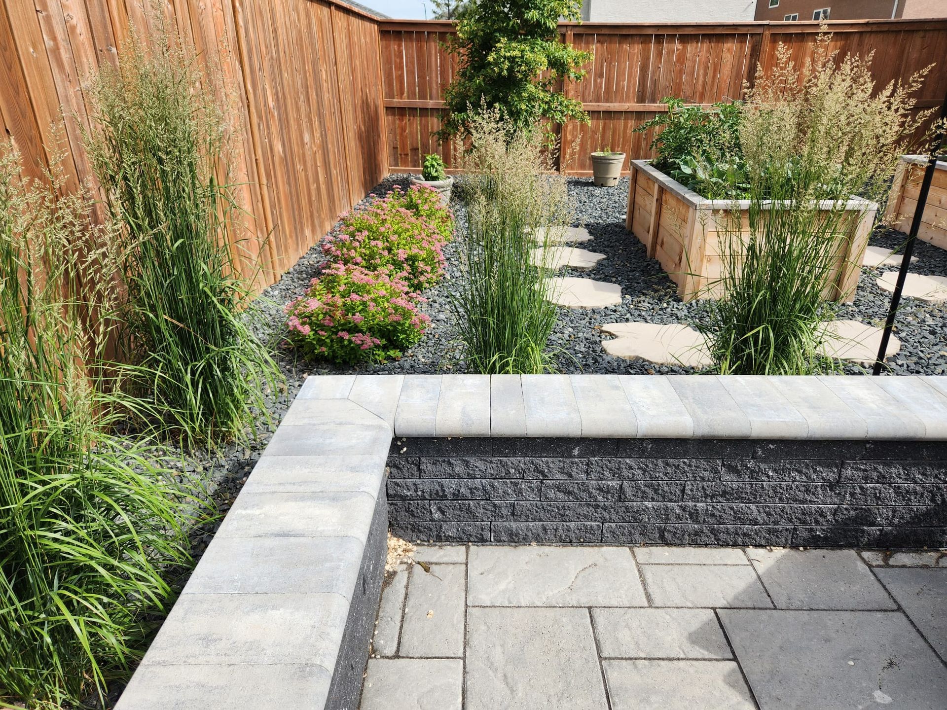A backyard with a wooden fence , planters , and a patio.