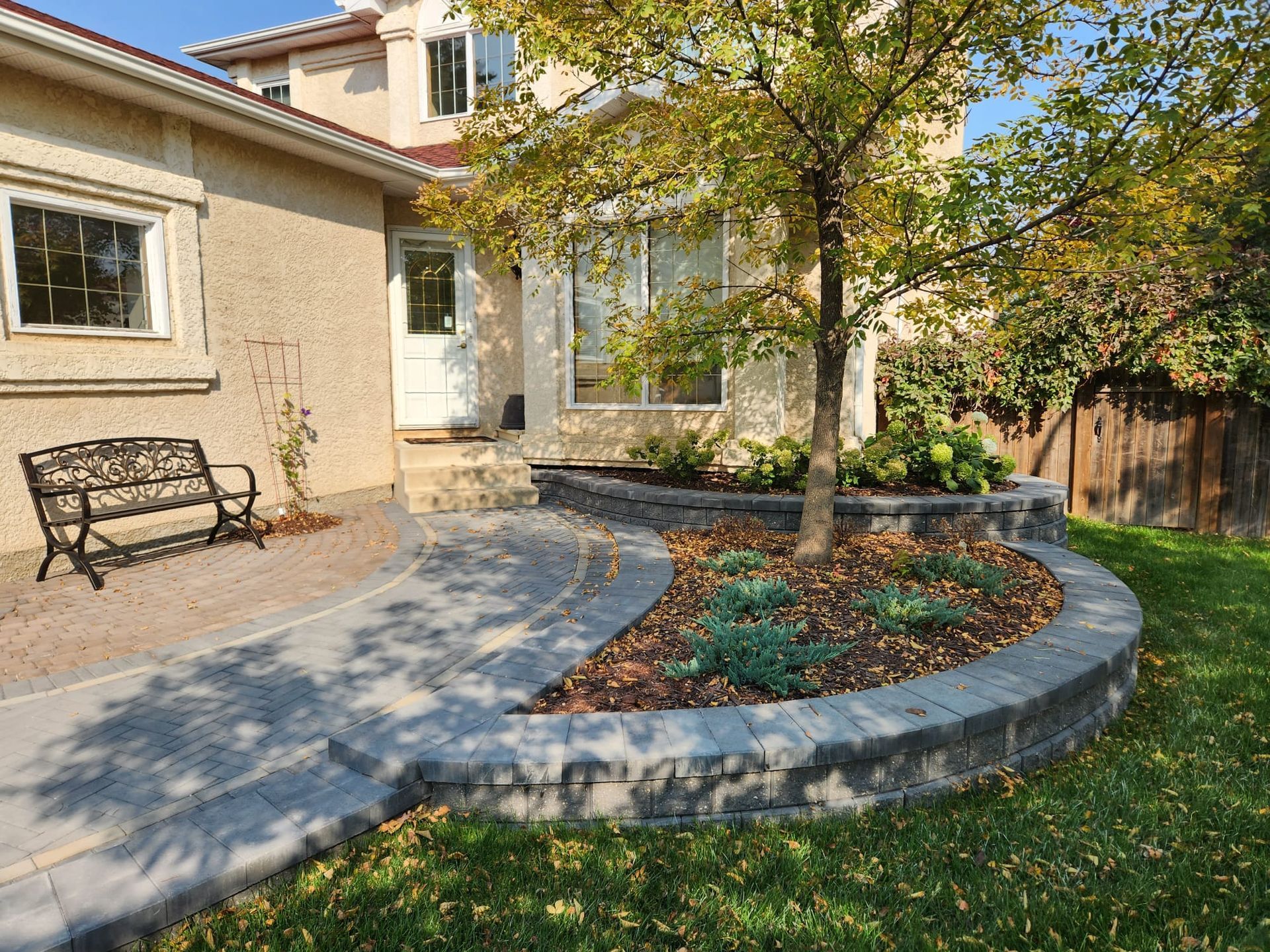 A patio with a bench and a tree in front of a house.
