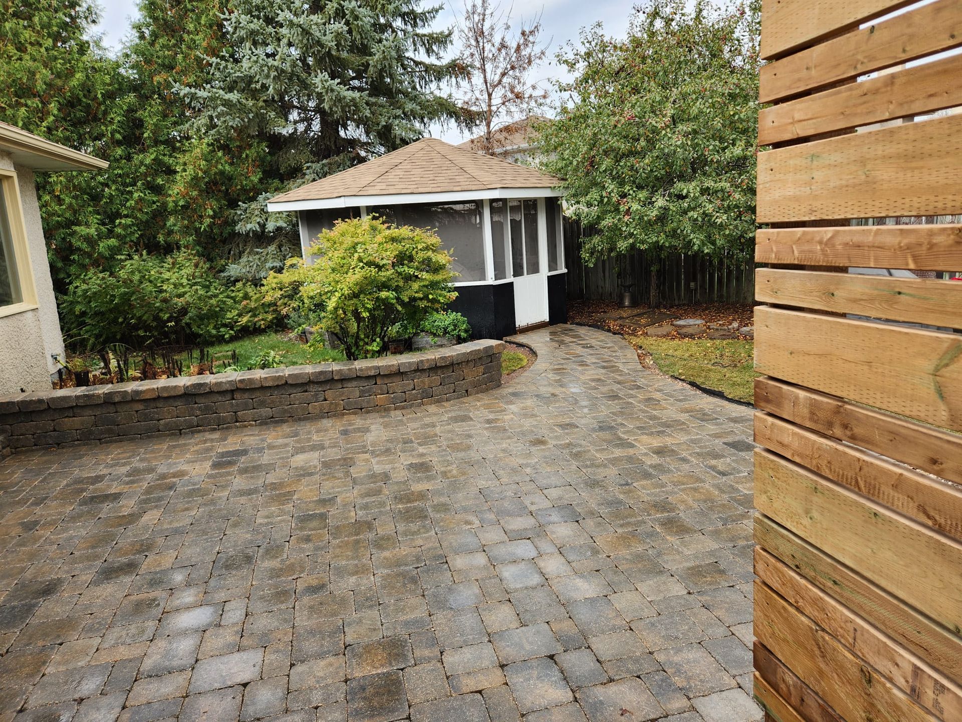 A paver patio leading to a house with a screened in porch.